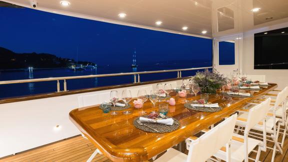 An elegantly laid dining table on the deck of the gulet 'Ugur' at night, with a view of the sea.